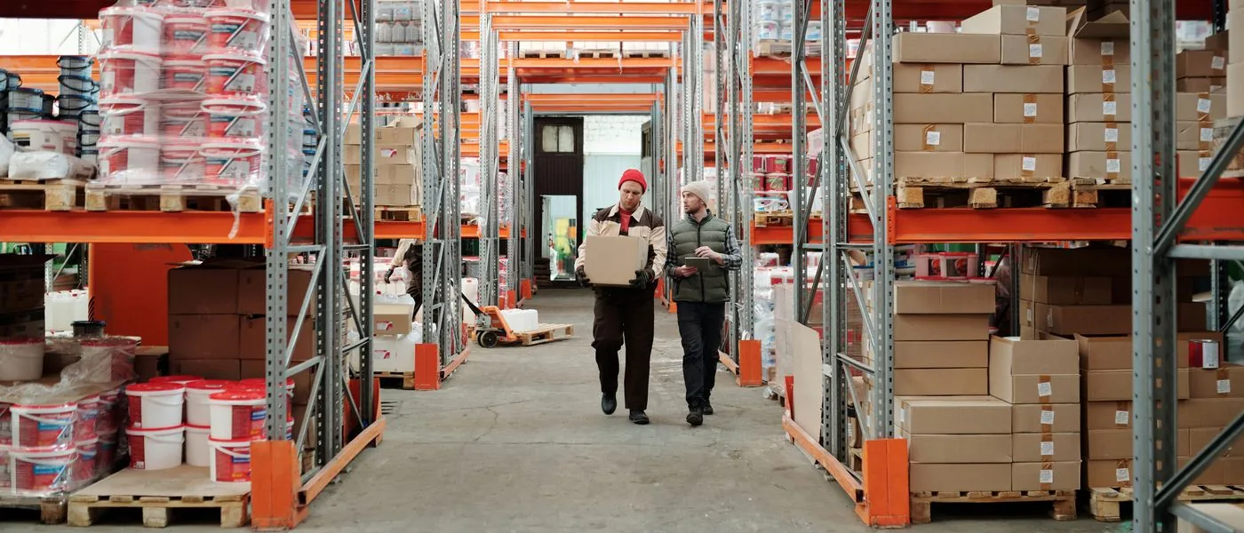 Two warehouse workers moving a case through the racked aisle of a food and beverage distribution center
